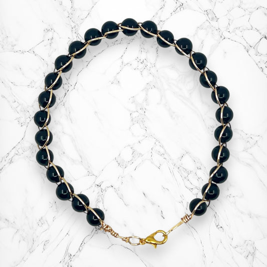 Black glass beads wrapped in gold-plated wire on a marble background